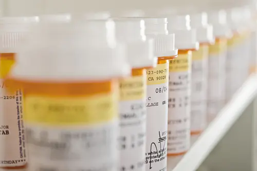 Row of prescription pill bottles with pharmacy labels on a shelf
